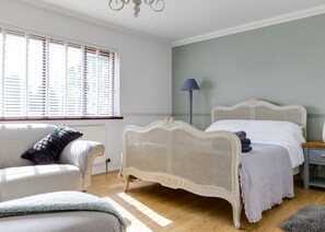 A bedroom with a white rattan bed, a grey sofa, and a floor lamp.