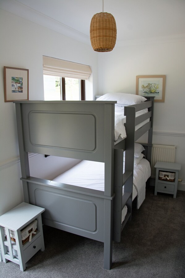 A bunk bed with a headboard, a bedside table with a drawer, a small nightstand, a wicker hanging light fixture, and two framed pictures on the wall.