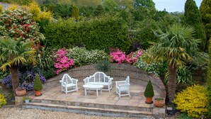 Une terrasse de jardin avec des meubles d’extérieur blancs et un mur en briques.