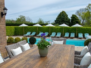 A poolside area with lounge chairs, umbrellas, and a wooden table with a potted plant.