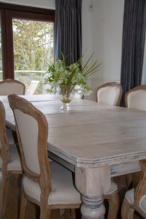 A dining table with a vase of flowers, surrounded by chairs with wooden frames and cushioned seats. - Hewas Water House with Pool, Hot Tub & Games Room (St Austell)