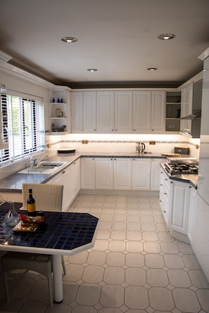 A kitchen with white cabinets, a hexagonal tile floor, and a dining area with a table and chairs. - Hewas Water House with Pool, Hot Tub & Games Room (St Austell)