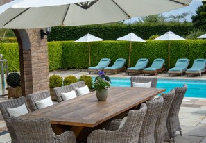 A poolside area with lounge chairs, umbrellas, and a wooden table with chairs.