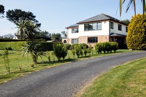 A two-story house with a paved driveway, surrounded by well-maintained hedges and a lawn.
