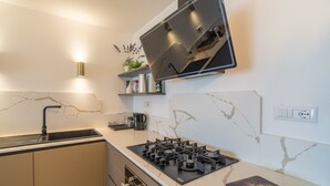 A kitchen with a gas stove, a sink, a countertop, and a wall-mounted TV. - Villa 'Coral Bay' with Sea View, Wi-Fi and Air Conditioning (Alghero)
