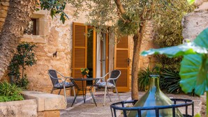 A stone building with wooden shutters, a small window, and a table with chairs outside.