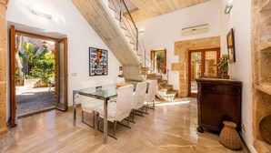 A spacious dining area with a glass table and chairs, a staircase, and a view of the outdoor garden.