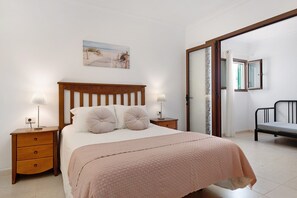 A bedroom with a bed, two bedside tables, a nightstand, a window with a view, and a door leading to another room.