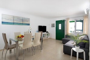 A modern living room with a dining area, a flat-screen TV, a green door, and a potted plant.