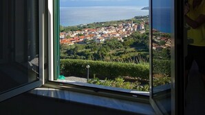 A room with a large window offering a view of a coastal town and the sea.