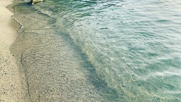 A beach with clear water, rocks, and a forested hillside.
