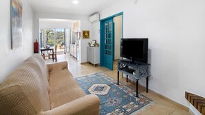 A living room with a sofa, a television on a stand, a patterned rug, and a blue door. - Country House 'Tibagota' with Mountain View, Wi-Fi and Air Conditioning (São Brás de Alportel)