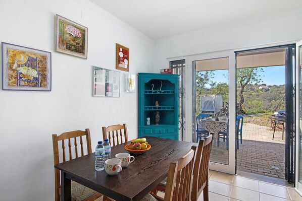 A dining area with a table, chairs, a water bottle, a bowl of fruit, and a teal cabinet.