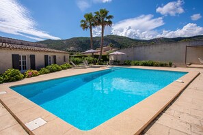 En rektangulær swimmingpool med en klar, blå vandoverflade, omgivet af en beige fliseterrasse.