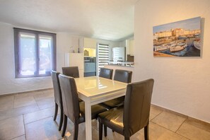 A dining area with a table and chairs, a kitchen in the background, and a painting on the wall.