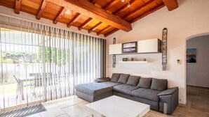 Een moderne woonkamer met een modulaire bank, een witte salontafel en een groot raam met zonwering.