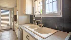 Een moderne keuken met twee spoelbakken, een raam met zonwering en een deur naar een andere kamer.