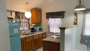 A compact kitchen with wooden cabinets, a blue refrigerator, a microwave, and a sink. - 08) The Marlin Cottage (Inglis)