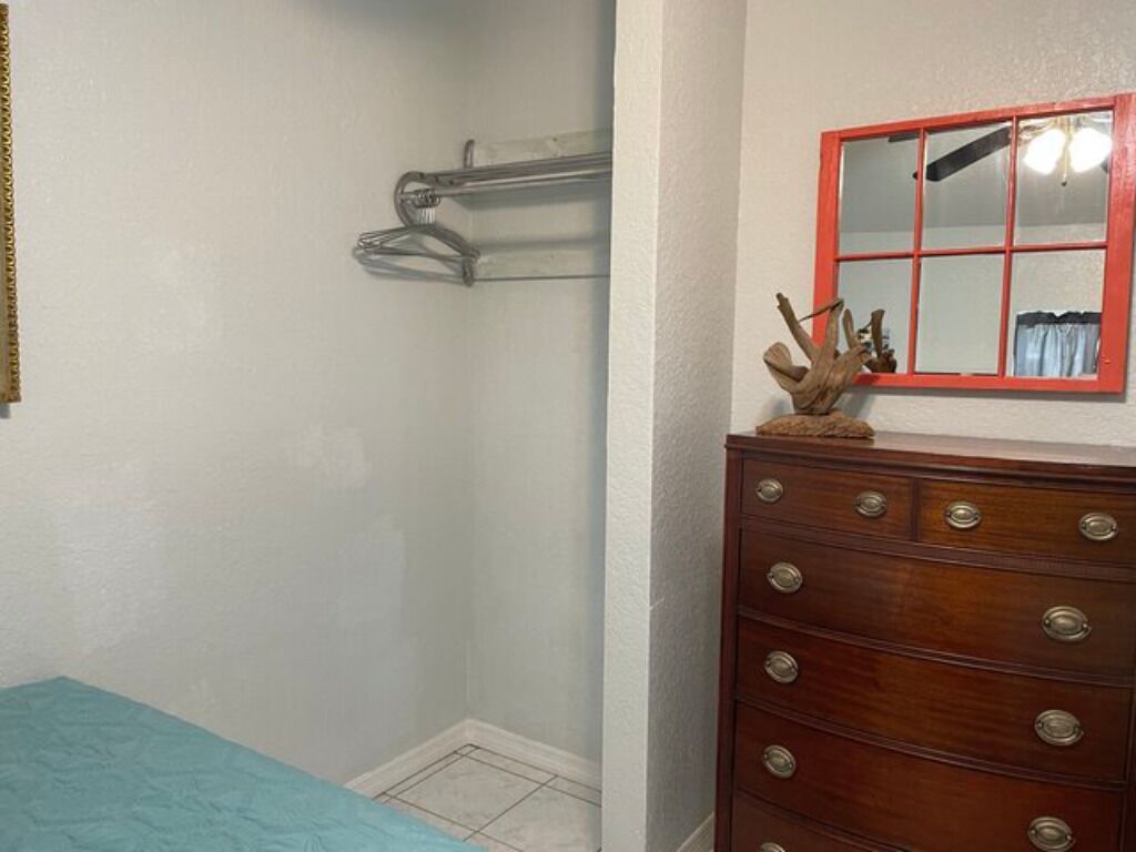 A room with a bed, a wooden dresser, a mirror with a red frame, and a coat rack.