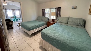 A bedroom with two beds, a ceiling fan, a window with curtains, and a door leading to another room. - 08) The Marlin Cottage (Inglis)