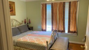 A bedroom with a bed, a bench, a nightstand, a lamp, and a window with curtains.