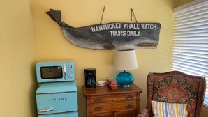 Une pièce avec un vieux réfrigérateur bleu, un meuble en bois, un fauteuil à motifs et un panneau mural sur lequel on peut lire : « Excursions quotidiennes d’observation des baleines à Nantucket ».