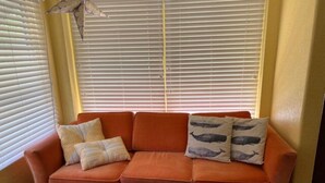 Une pièce avec un canapé placé devant une fenêtre munie de stores, une décoration murale et un tapis à motifs.