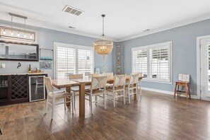 A dining area with a wooden table and chairs, a chandelier, and large windows with blinds. - Sojourn Baycation 4 BR House 5 Min walk to Beach (Norfolk)