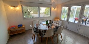 Uma área de refeições com mesa posta para quatro pessoas, rodeada por cadeiras, um banco com livros e um radiador.