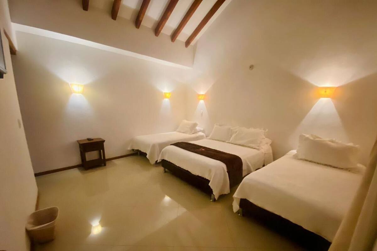 Una habitación con dos camas, una mesita pequeña y luces fijadas en la pared.