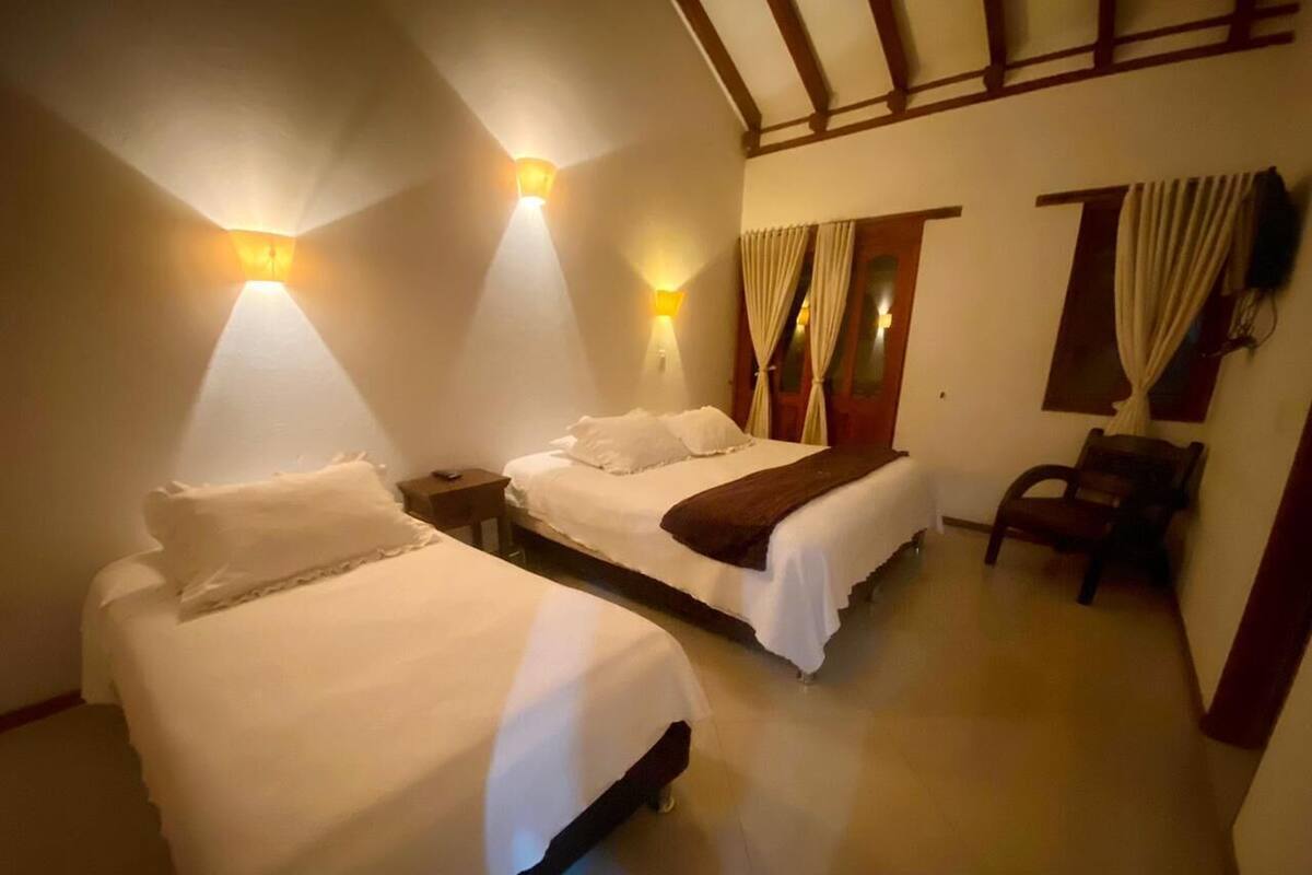 Habitación de hotel con dos camas, techo de madera y una silla.