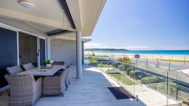 Ein Balkon mit Esstisch und Stühlen, mit Blick auf einen Strand.