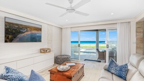 Ein modernes Wohnzimmer mit großem Fenster und Blick auf den Strand, einem Deckenventilator und einer gemütlichen Sitzecke.