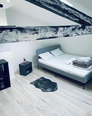 A modern bedroom with a grey bed, white pillows, a small black nightstand, and a grey rug.