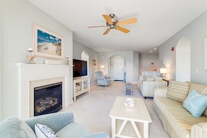 A living room with a fireplace, a ceiling fan, a television, and striped furniture.