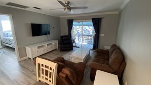 Una sala de estar con televisión de pantalla plana, ventilador de techo, sofá, mesa de centro y una silla.
