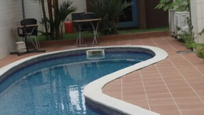 A swimming pool with a tiled edge, surrounded by a patio area with chairs and plants. - Residence Jireh  (Abidjan)