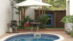 A swimming pool with a tiled deck, surrounded by a small patio area with a table and chairs. - Residence Jireh  (Abidjan)
