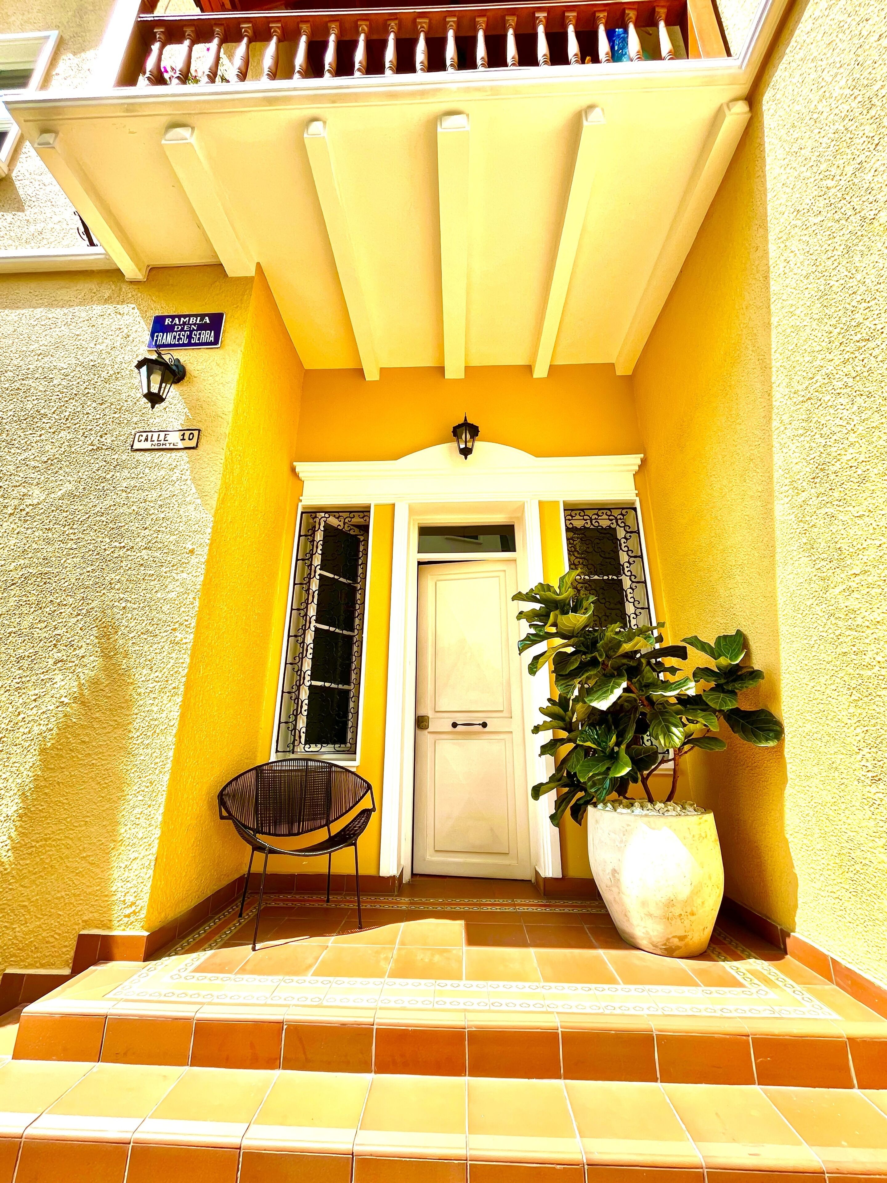 Un edificio giallo con una porta bianca, una pianta in vaso e una sedia all'esterno.