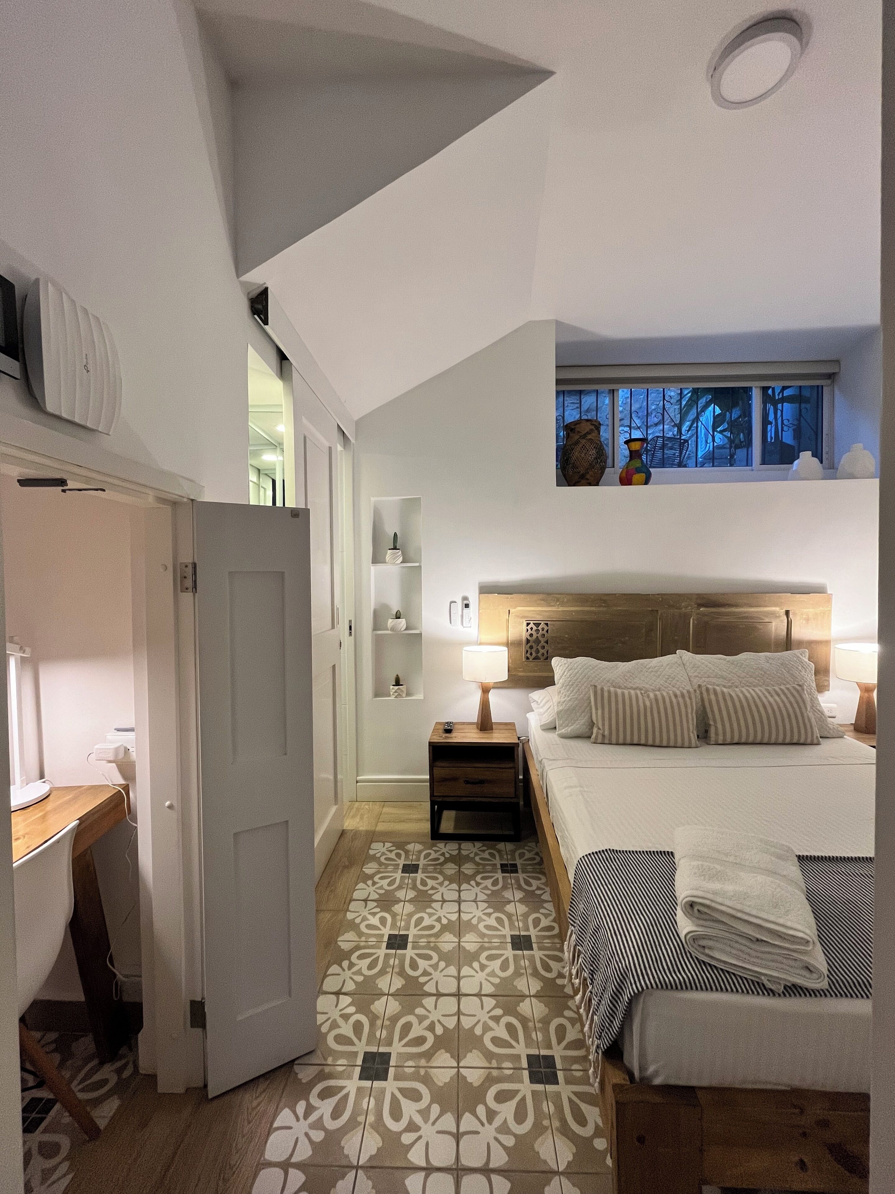 Una camera da letto con un letto, un comodino, una lampada e una finestra vista alberi.