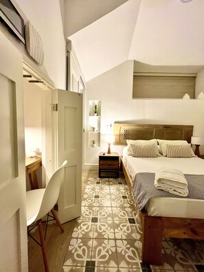 Un dormitorio con cama, mesita de noche, lámpara, silla y suelo estampado.