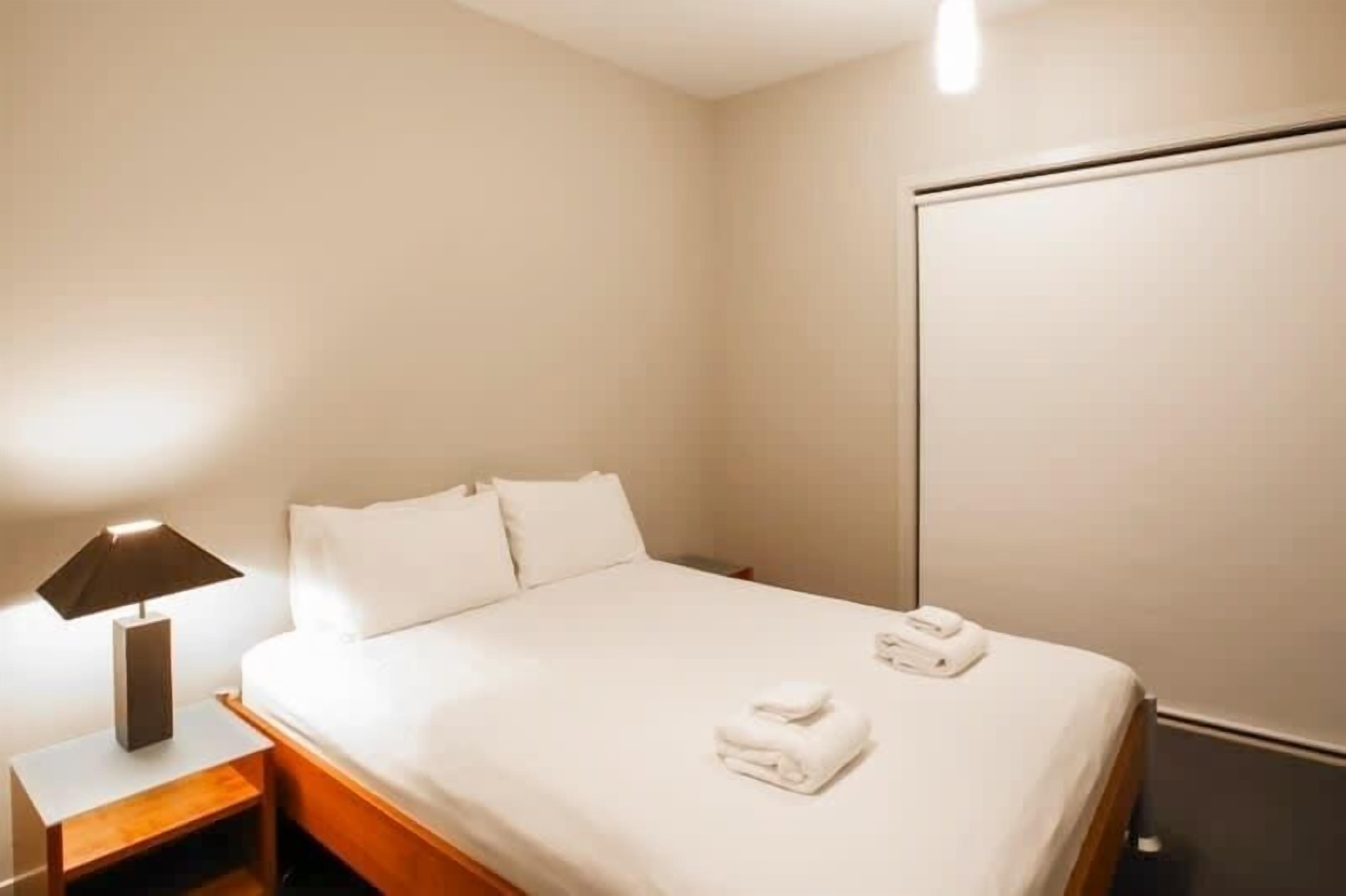 A hotel room with a bed, a nightstand with a lamp, and a wardrobe.