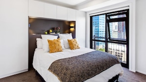 Un dormitorio moderno con una cama grande, espacio de almacenamiento integrado, vista a la ciudad y un ventanal amplio.