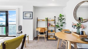 Una sala de estar moderna con una mesa de comedor de madera, un sillón amarillo, una estantería y un amplio ventanal con vistas a la ciudad.