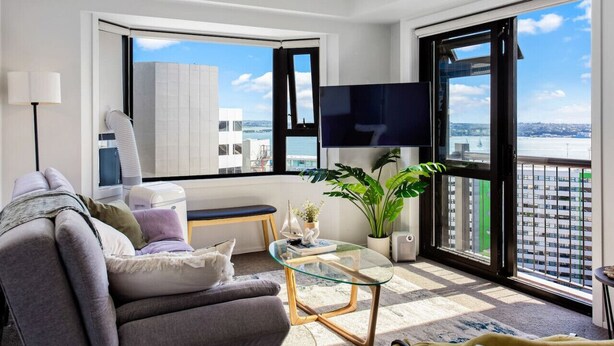 Una sala de estar moderna con un sofá, una mesa de centro de vidrio, un televisor y un ventanal con vista a la ciudad.