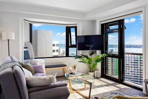 Una sala de estar moderna con un sofá, una mesa de centro de vidrio, un televisor y un ventanal con vista a la ciudad.