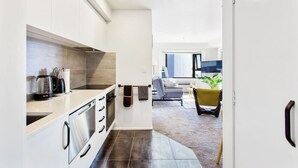 Una cocina moderna con armarios blancos, una cafetera y un sofá gris en la sala de estar.