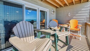 A covered outdoor seating area with Adirondack chairs and a table, overlooking the ocean.