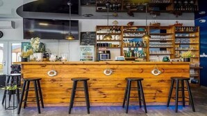 Un espace bar avec un comptoir en bois, des tabourets noirs et des étagères remplies de bouteilles et de verres.