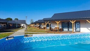 Un espace moderne aménagé au bord de la piscine, avec une piscine à l’eau d’un bleu limpide, des coins salon abrités et un chemin menant à la piscine.